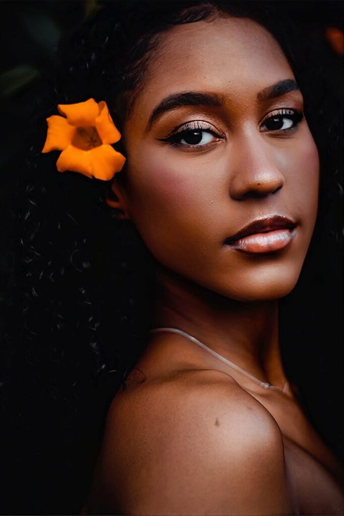 Close-up portrait of a woman with dark hair and orange flower accentuating beauty.