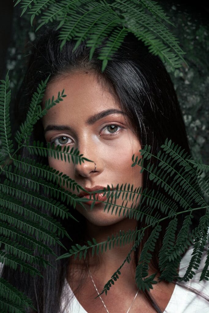 Close-up portrait of a woman behind green fern leaves, portraying natural beauty.