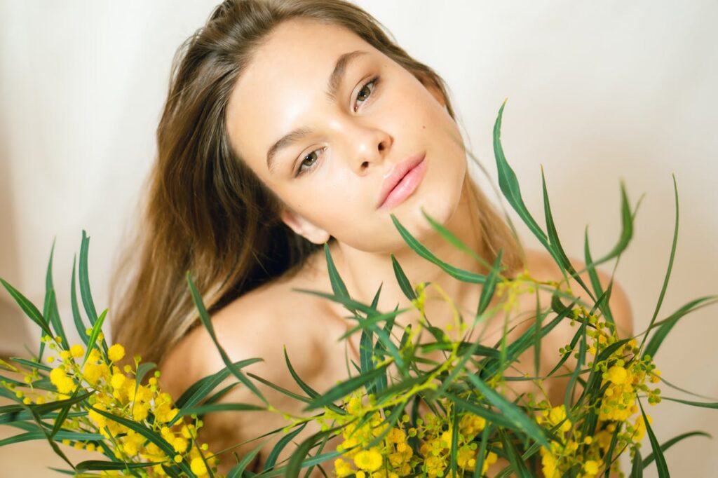 A young woman poses gracefully with yellow mimosa flowers in a studio setting.