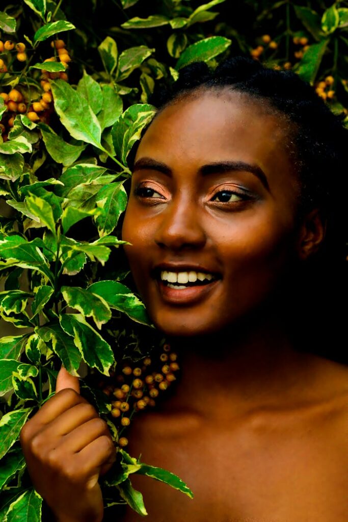A beautiful woman smiling amidst vibrant green foliage and berries, captured outdoors in Nairobi.