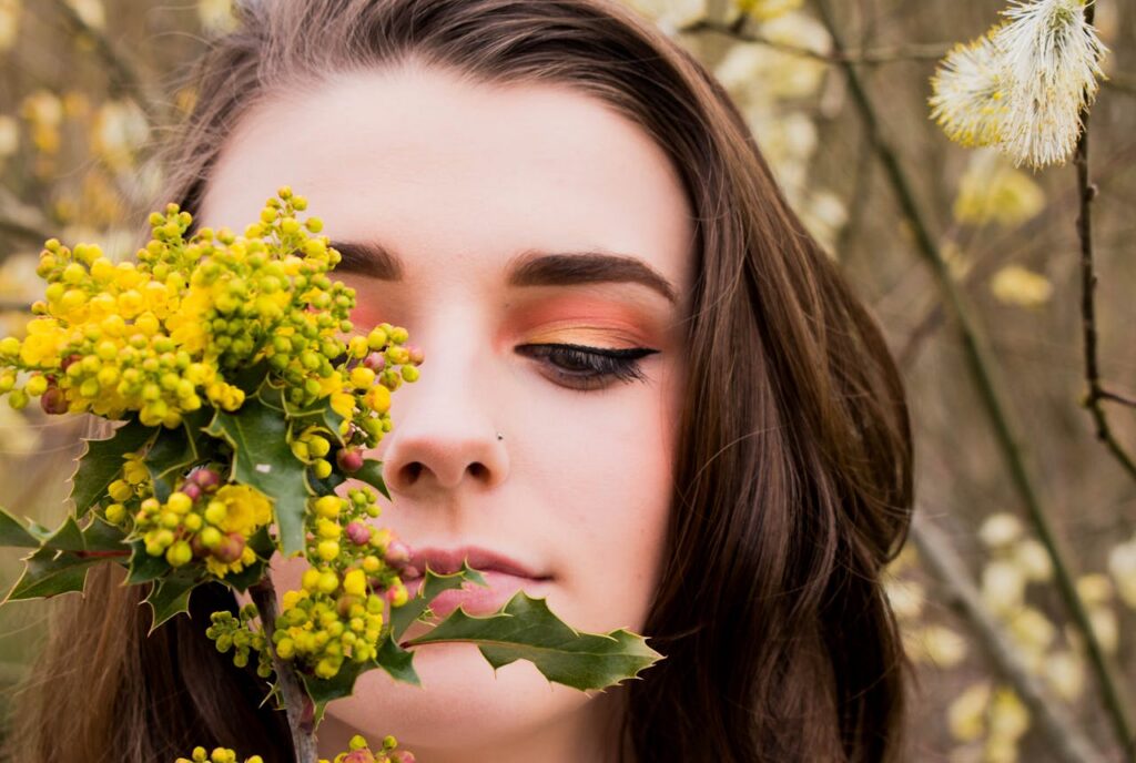 Close-up portrait of a woman with bright eye makeup surrounded by spring flowers.
